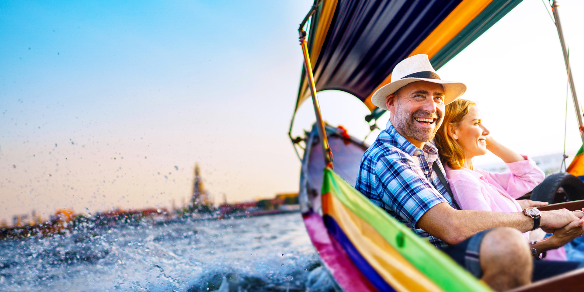 middle-aged man and woman snuggling with big smiles in brightly colored boat on the sea at sunset