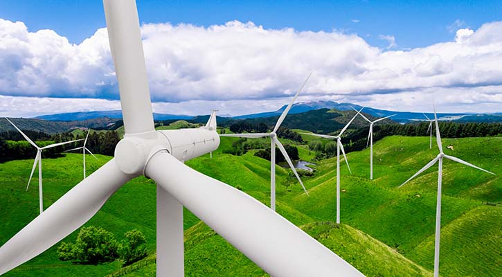  A windmill farm set in green hills with mountains in the distance and a cloudy sky.